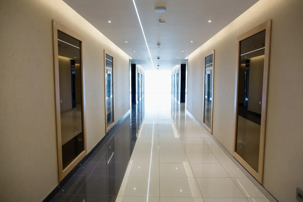 Couloir moderne et lumineux avec carrelage brillant et éclairage encastré, desservant des portes en bois et des miroirs muraux, dans un bâtiment professionnel